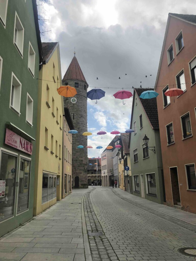 Marktstraße in Gunzenhausen mit Blick auf den Turm. Die Straße ist mit bunten Regenschirmen geschmückt.