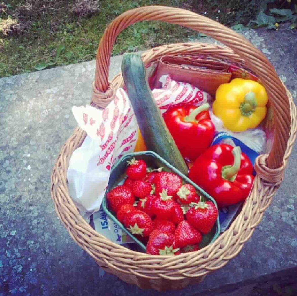 Einkaufskorb mit frischen Gemüse wie Gurke, Paprika rot und gelb sowie eine Schale frische Erdbeeren. 