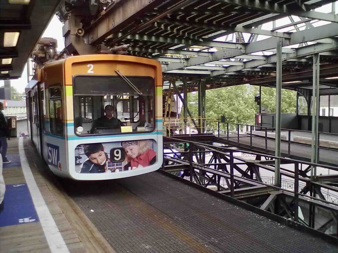 Wuppertaler Schwebebahn: Eine bunt bedruckte Gondel bei der Einfahrt in eine Haltestelle.