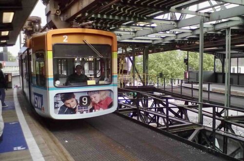 Wuppertaler Schwebebahn: Eine bunt bedruckte Gondel bei der Einfahrt in eine Haltestelle.