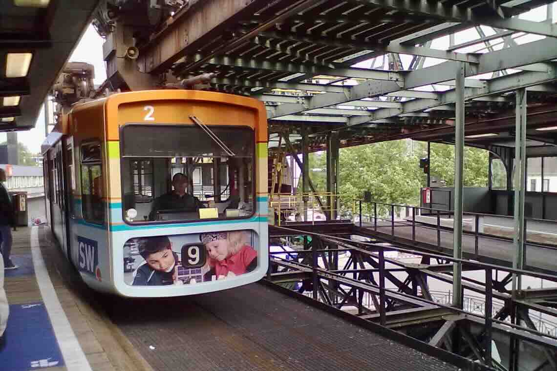 Wuppertaler Schwebebahn: Eine bunt bedruckte Gondel bei der Einfahrt in eine Haltestelle.